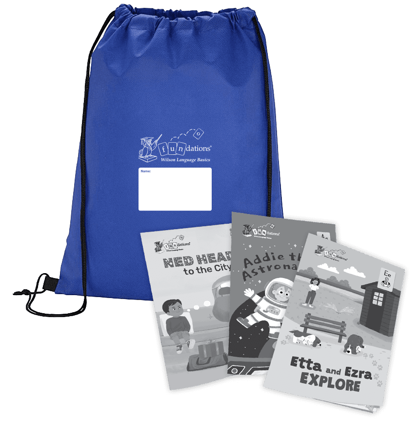 A royal blue Fundations® drawstring backpack with black cords and a white label for writing a name, shown alongside three illustrated children’s readers titled Ned Heads to the City, Addie the Astronaut, and Etta and Ezra Explore. The books are spread in front of the backpack and display black-and-white cover illustrations.