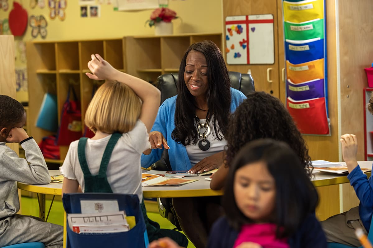 Student with hand raised and teacher smiling at them