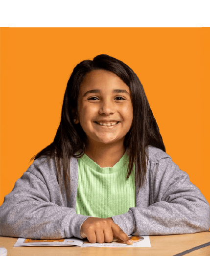 Smiling girl sits at a desk, pointing to a page in front of her, with an orange background behind her.