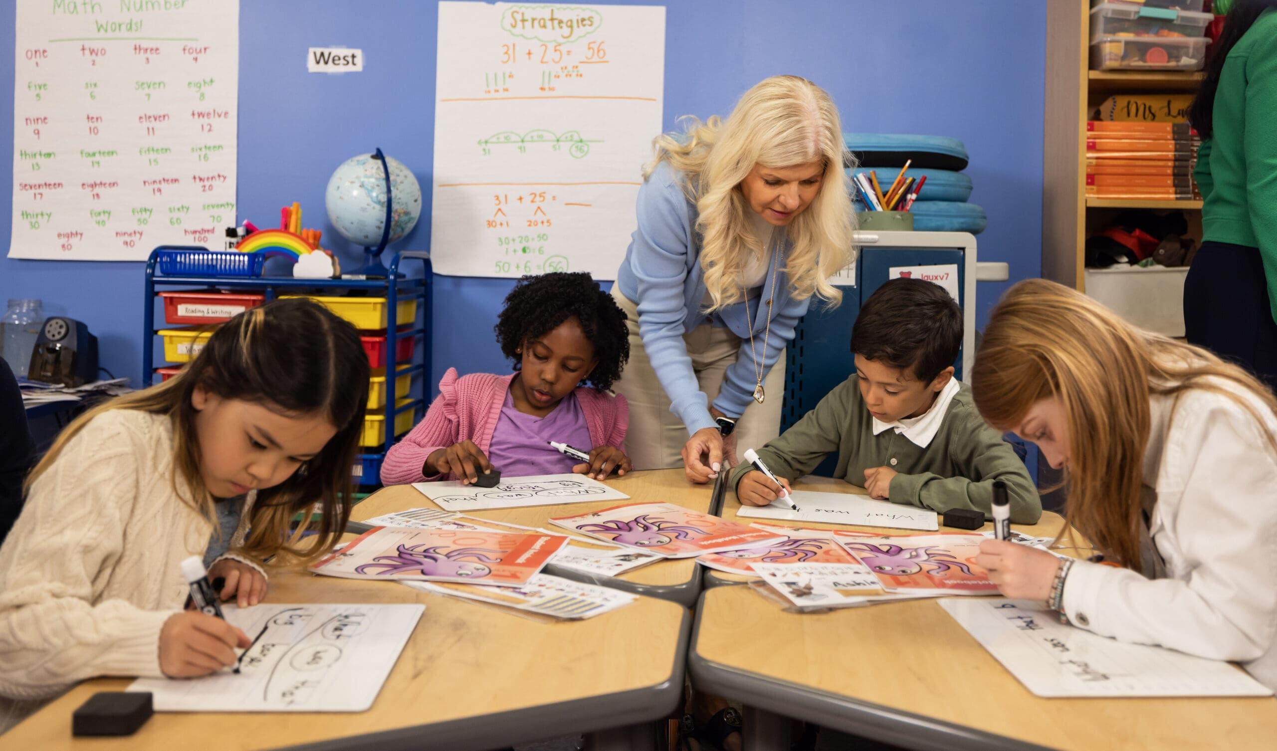 Teacher helping elementary students with math at a table in a classroom.