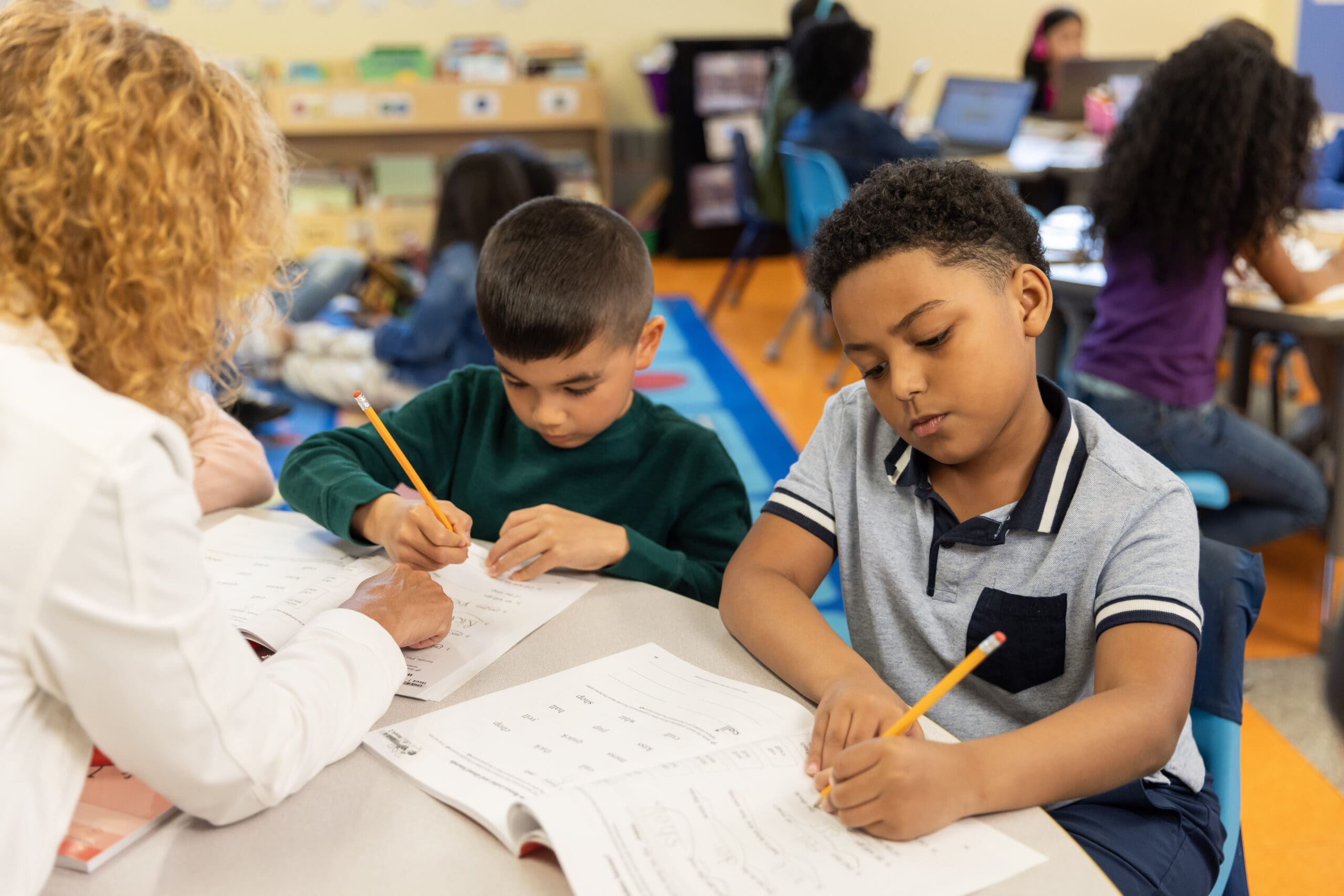 Elementary students working on Fundations K-3 workbook with teacher assistance in a classroom setting.
